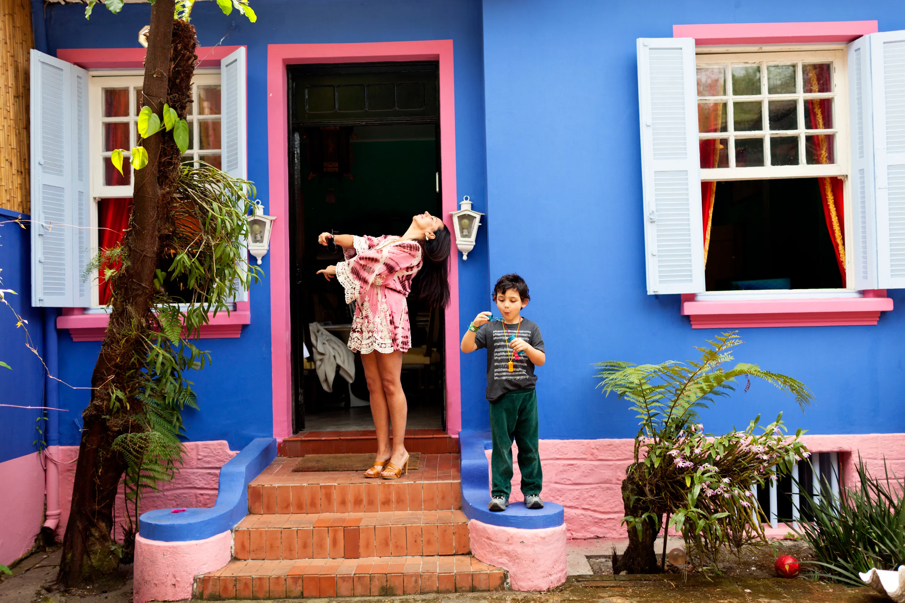 A mother and son on the front steps of their colorful blue and pink home