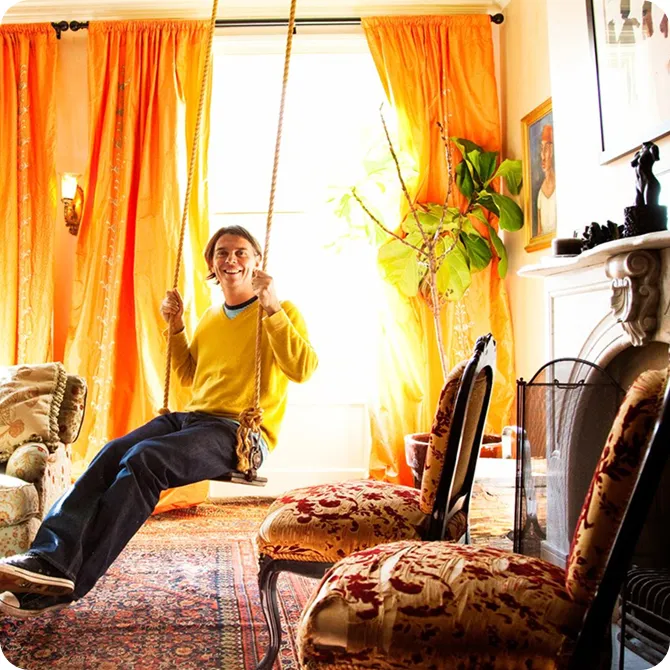 A homeowner on an indoor rope swing in a warm, sunlit room with orange curtains